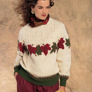 May include: A cream-colored long-sleeve knit sweater featuring a textured yoke pattern, a horizontal band of red and green maple leaf motifs across the chest, and a solid dark green ribbed hem and cuffs. The text PDF File Pattern is visible.