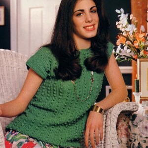 May include: A green crochet top with a textured pattern. The top has short sleeves and a round neckline. The image also shows a floral skirt and a gold bracelet. The text "PDF File PATTERN" is visible in the upper left corner.