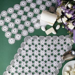 Pode incluir: Dois naperons de croché de crochê brancos com um motivo floral circular repetitivo e uma borda festonada intrincada. A imagem inclui o texto PDF File Pattern. Os naperché são exibidos ao lado de flores brancas, uma pequena caixa e doces brancos.