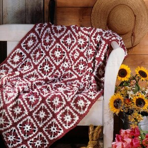 May include: A crochet blanket featuring a repeating diamond pattern in deep burgundy and white yarn. The textile is draped over a white chair and includes the text PDF File Pattern in the upper left corner of the image.