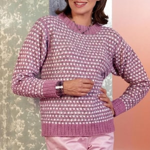 Może przedstawiać: Kobieta w różowo-białym swetrze we wzory. Sweter ma okrągły dekolt i długie rękawy ze ściągaczami. Tekst "CROCHET PDF PATTERN" znajduje się w białym okręgu. Ma również na sobie różowe spodnie.