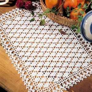 May include: A rectangular white crochet doily featuring an intricate openwork pattern with a delicate scalloped edge. The textile is crafted with fine thread, showcasing a repeating geometric design that creates a light, airy appearance.