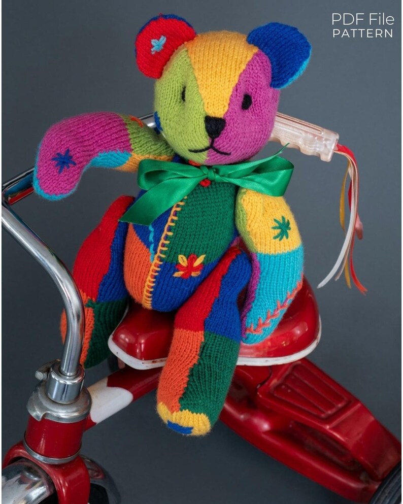 May include: A multi-colored knitted teddy bear featuring a patchwork design in red, green, yellow, blue, and purple yarn with embroidered star accents and a green satin ribbon tied around its neck. The text PDF File PATTERN is visible.