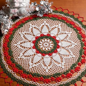 May include: A round, crocheted doily featuring a complex, circular pattern in white, dark green, and red yarn. The design includes intricate floral-like motifs and a delicate, open-work border, creating a detailed, lace-like textile piece.
