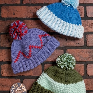 May include: Three knitted beanies with pom-poms. One is blue with a light blue brim, one is purple with a red zigzag pattern and red-purple pom-pom, and one is olive green with a light green stripe and brim. A circular patch reads CAPS FOR KIDS.