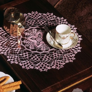 May include: A vintage tea setting on a dark wood table. A pink crocheted doily supports a floral teacup and saucer with a silver spoon. A silver teapot is next to the doily. A plate of breadsticks is in the foreground.