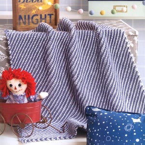 May include: A navy blue and white striped throw blanket is draped over a shelf. A Raggedy Ann doll sits in a red wagon. A blue pillow with a white star pattern is on the right. A wooden sign with the words "Good Night" is in the background.