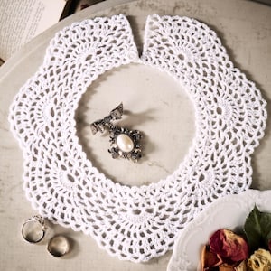 May include: A white, crocheted collar with a delicate, openwork design. A vintage brooch with a pearl-like center and two rings are placed inside the collar. The text "PDF File PATTERN" is visible in the upper right corner.