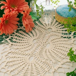 May include: An off-white oval crochet doily featuring an intricate openwork pattern with fan-like motifs and a scalloped edge. The delicate textile is crafted with fine thread, showcasing a symmetrical design that radiates from the center outward.