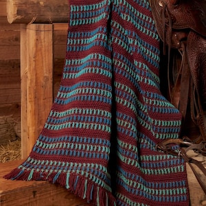 May include: A rectangular crochet blanket featuring alternating horizontal stripes of deep maroon, bright turquoise, and royal blue yarn. The textile has a textured stitch pattern throughout and is finished with short, matching maroon and turquoise fringe.