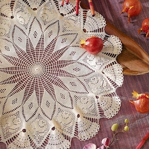 May include: A round, off-white crocheted doily featuring a complex, radiating starburst pattern with intricate diamond-shaped cutouts and a scalloped edge. The textile displays a fine, thread-like construction with a symmetrical, geometric design.