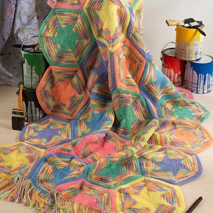 May include: A handmade crochet blanket featuring a repeating pattern of multicolored hexagonal motifs in shades of pink, yellow, green, orange, and blue. The blanket has a fringed edge and is constructed from variegated yarn with a textured stitch.