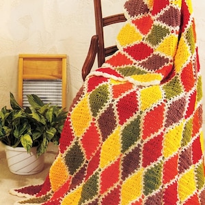 May include: A handmade crochet blanket featuring a repeating diamond pattern in vibrant shades of red, yellow, orange, and dark green, with each diamond shape outlined in a cream-colored yarn border, creating a textured and colorful textile design.