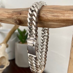 May include: A silver chain bracelet with a clasp fastening. The bracelet is made of a thick, interwoven chain.