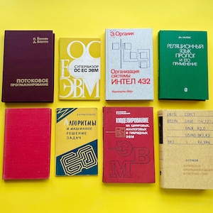Puede incluir: Una colección de ocho libros de tapa dura con cubiertas de varios colores, incluyendo granate, amarillo, gris claro, verde, rojo y beige. Los libros presentan texto en cirílico, con un libro beige que muestra código de ensamblaje técnico.