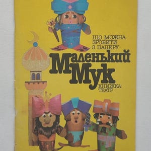 Puede incluir: Una portada de libro infantil vintage con fondo amarillo. La portada presenta ilustraciones de muñecos de papel y el título "Маленький Мук" en letras grandes y estilizadas. También hay texto adicional en ucraniano.