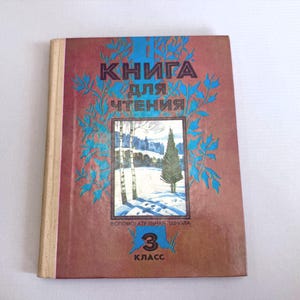 May include: Vintage book with a brown cover featuring Russian text and a winter landscape illustration. The cover has blue floral accents and the text "КНИГА ДЛЯ ЧТЕНИЯ" (Book for Reading). The book is marked "3 КЛАСС" (3rd Grade).