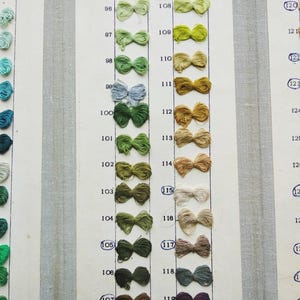 May include: A vintage color chart displaying a range of thread colors. Each color is presented as a small, tied bow, arranged in vertical columns. The colors vary from greens and blues to browns and tans, with numbers next to each sample.