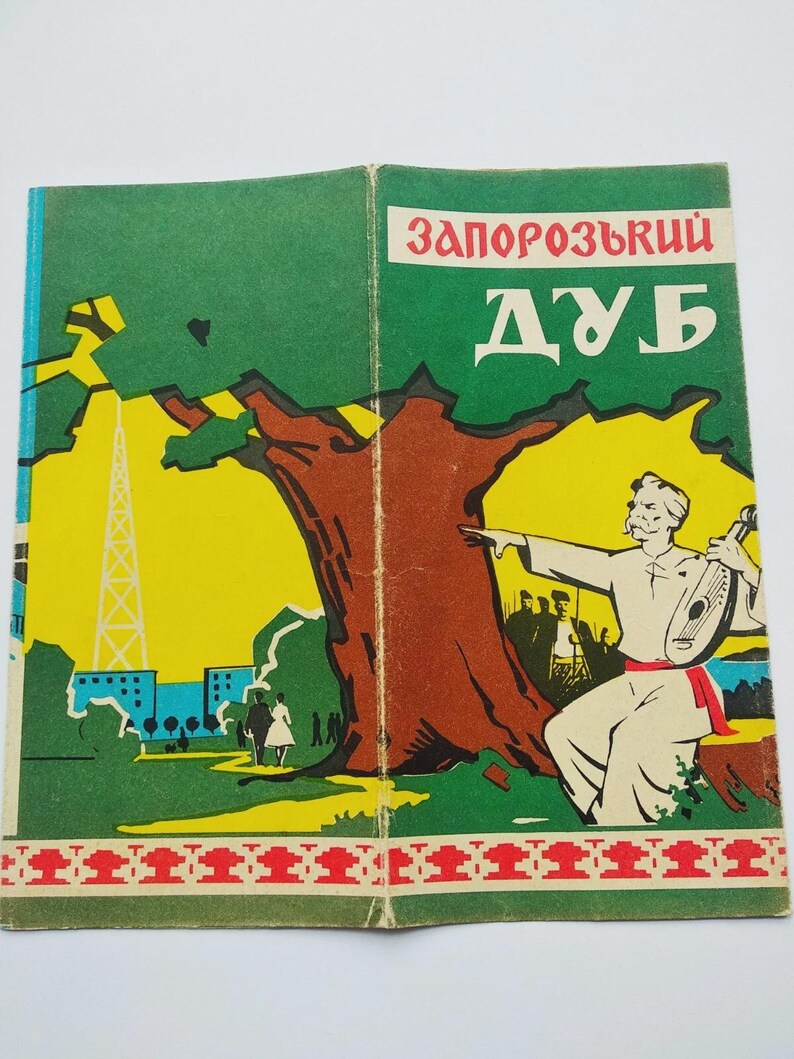 May include: Vintage book cover featuring a colorful illustration. The cover displays the title "Zaporozhskyi Dub" in red and white text. The artwork depicts a tree, a man playing a stringed instrument, and a landscape with buildings and a tower.