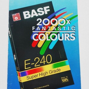 May include: A vintage BASF E-240 VHS videocassette with "2000x Fantastic Colours" text. The black cassette has a yellow and gold "Super High Grade" label. The packaging is blue with Russian text.