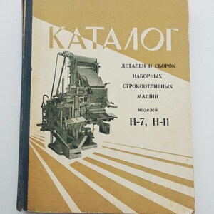 Może przedstawiać: Katalog w stylu vintage z tytułem "KATALOG" w złotych literach. Okładka zawiera szczegółową ilustrację prasy drukarskiej i tekst w języku rosyjskim. Katalog jest oprawiony w ciemnoniebieski grzbiet i ma beżowo-białe tło.