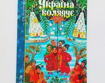 May include: A colorful book cover featuring a winter scene with a group of people in traditional clothing. The title "Україна колядує" is displayed in green and yellow. The cover has a blue border with snowflakes.