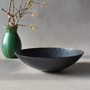 May include: A black, hammered metal bowl with a slightly rounded rim. The bowl has a textured surface and the number "17" is engraved on the bottom.