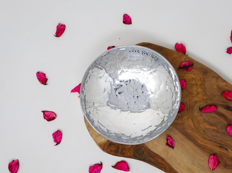 Beautiful Aluminium Hammered Bowl. Silver and reflective. Stamped with the text Love you Lots. Displayed on a rustic piece ofwood surrounded with dried pink rose petals. 10th anniversary personalised wedding gift.