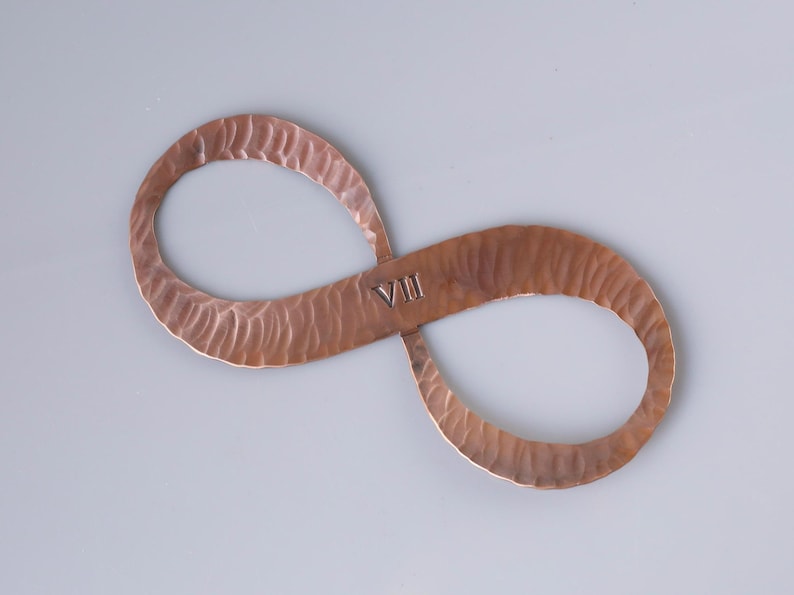 May include: A copper-colored infinity symbol with a hammered texture. The Roman numeral "VIII" is stamped in the center. The symbol is displayed on a light gray background.