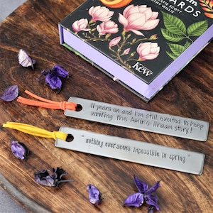 May include: Two silver metal bookmarks with orange and yellow tassels. The bookmarks have engraved text that reads "II years on and I'm still excited to keep writing the Amir & Ilhaam story!" and "nothing ever seems impossible in spring."