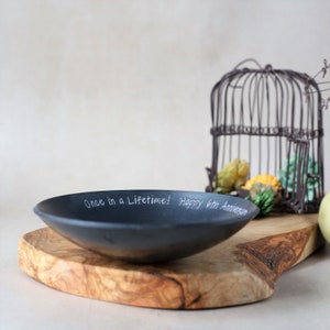 May include: A black slate bowl with the inscription "Once in a lifetime! Happy 6th Anniversary" sits on a wooden cutting board.