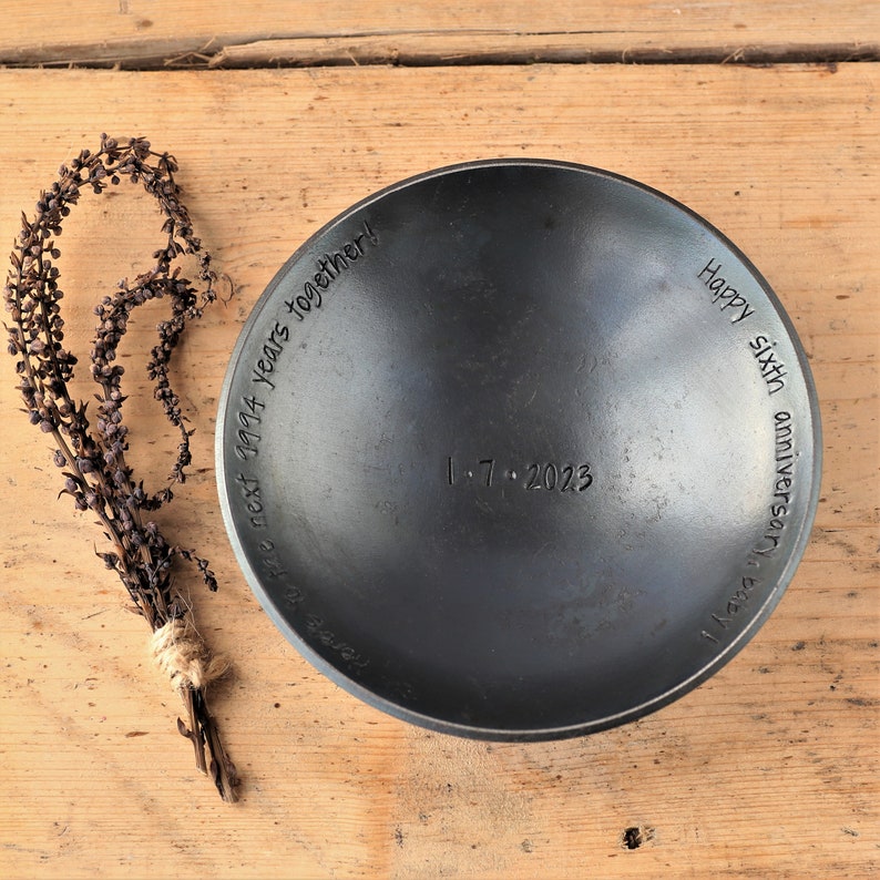 May include: A black metal bowl with the inscription "Happy sixth anniversary! The next 9994 years together! 1.7.2023"