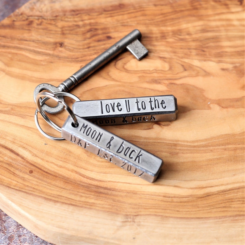 May include: Two silver metal keychains with engraved messages. The top keychain says "love U to the moon & back". The bottom keychain says "Moon & back D&F Est. 2017".