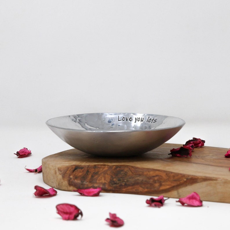 Beautiful Aluminium Hammered Bowl. Silver and reflective. Stamped with the text Love you Lots. Displayed on a rustic piece ofwood surrounded with dried pink rose petals. 10th anniversary personalised wedding gift.