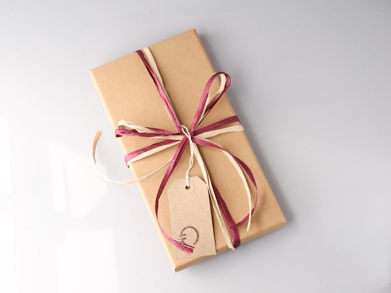 May include: A rectangular gift box wrapped in brown paper, tied with burgundy and cream-colored ribbons. A small, light brown tag hangs from the ribbon, with a simple design. The overall presentation is neat and elegant.