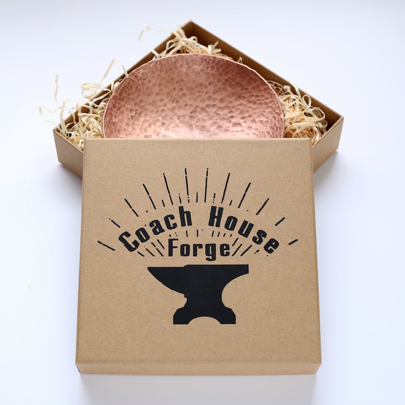 May include: A hammered copper bowl sits in a brown cardboard box with the words "Coach House Forge" and an anvil logo printed on the box.