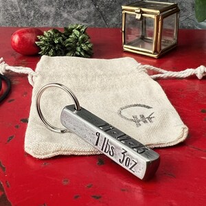 May include: A silver metal keychain with a rectangular bar engraved with "9 lbs 3oz". The keychain is on a white fabric pouch with a small circle logo.