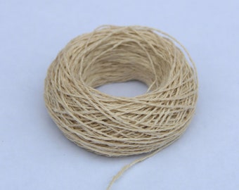 May include: A close-up of a ball of natural fiber twine, wound into a neat circle. The twine is a light beige color and has a rough texture.