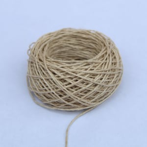 May include: A ball of natural twine, made from a natural fibre, is wound into a neat circle. The twine is a light beige colour and has a rough texture. A long strand of twine is hanging from the ball.