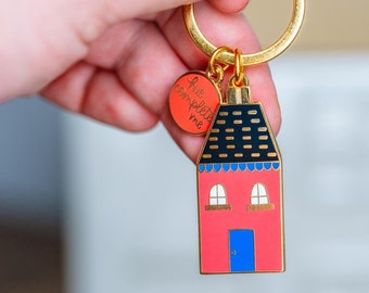 May include: A gold-colored keychain with a red house charm, blue door, and black roof. The keychain also features a round red charm with the words "true complete me".