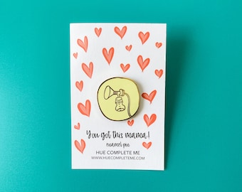 Könnte beinhalten: Gelber Emaille-Pin mit einem Brustpumpen-Design, auf einer weißen Karte mit orangefarbenen Herzen. Die Karte trägt den Text "You got this mama!" und eine Website-Adresse.