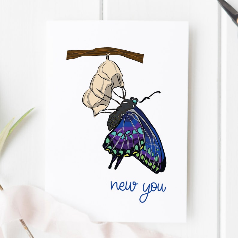 May include: A greeting card with a blue and purple butterfly emerging from a white cocoon. The card has the text "new you" written in blue.