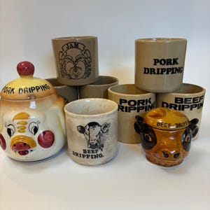 May include: A selection of vintage ceramic kitchen storage items. The image shows jars and containers with illustrations of a cow, a pig, and fruit, with text including "Pork Dripping" and "Beef Dripping". The colors are beige, brown, and yellow.