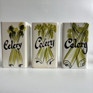 May include: Three cream-coloured ceramic containers, each with a green and yellow celery illustration and the word "Celery" in black script. These rectangular containers are likely for kitchen storage, adding a vintage touch.