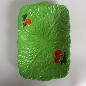 May include: A rectangular, green ceramic serving platter shaped like a lettuce leaf. The platter has embossed leaf veins and is decorated with two sets of red tomatoes and green leaves.
