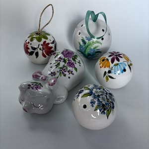 May include: A selection of white ceramic ornaments, including spheres and a pig figurine, decorated with hand-painted floral patterns in multiple colours. Some pieces have holes and ribbons for hanging.