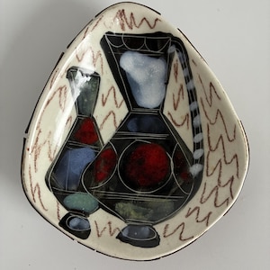 May include: A ceramic, triangular dish with a cream background and a black border. It features two stylized vase designs in black, red, blue, and green. The background has a brown, wavy pattern.