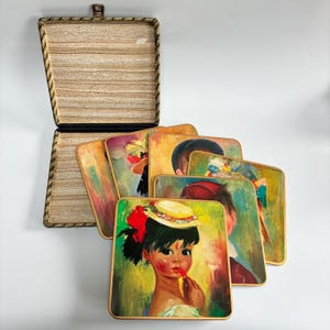May include: A collection of vintage coasters with painted portraits, including a young girl applying lipstick. The square coasters have rounded corners and a wooden frame. They are stored in a matching wooden box with a hinged lid.