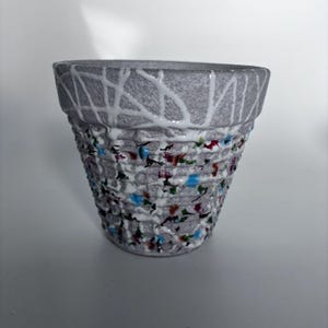 May include: A grey ceramic plant pot with a textured surface. The pot has a white, web-like design around the rim and colourful accents of blue, red, and green. The pot is designed for planting flowers or herbs.