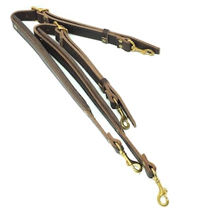 May include: A brown leather camera strap with two brass hooks and a double strap design.